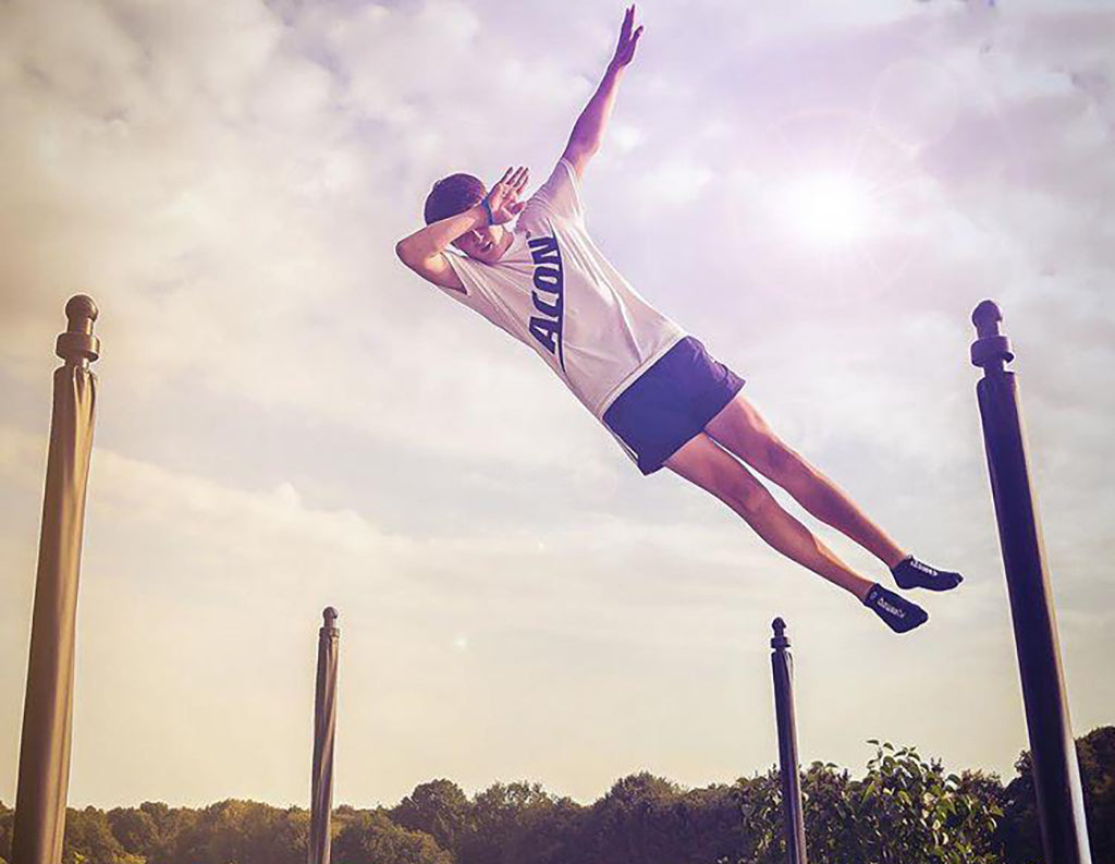 Mies hyppii trampoliinilla ACON logo t-paita päällä.