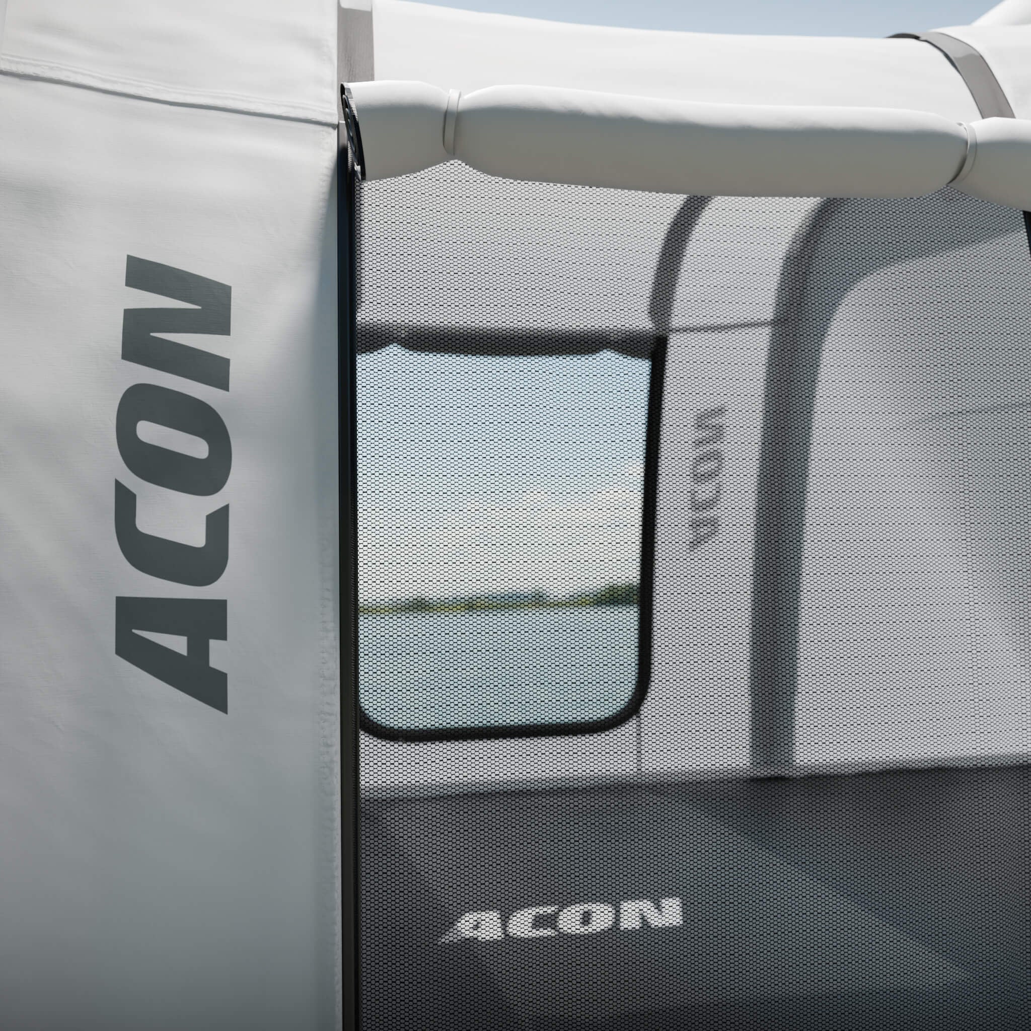 Lähikuva avoimesta Acon Trampoliiniteltan ovesta teltan sisätiloihin. Oven vieressä valkoisessa telttakankaassa on harmaa Aconin logo.