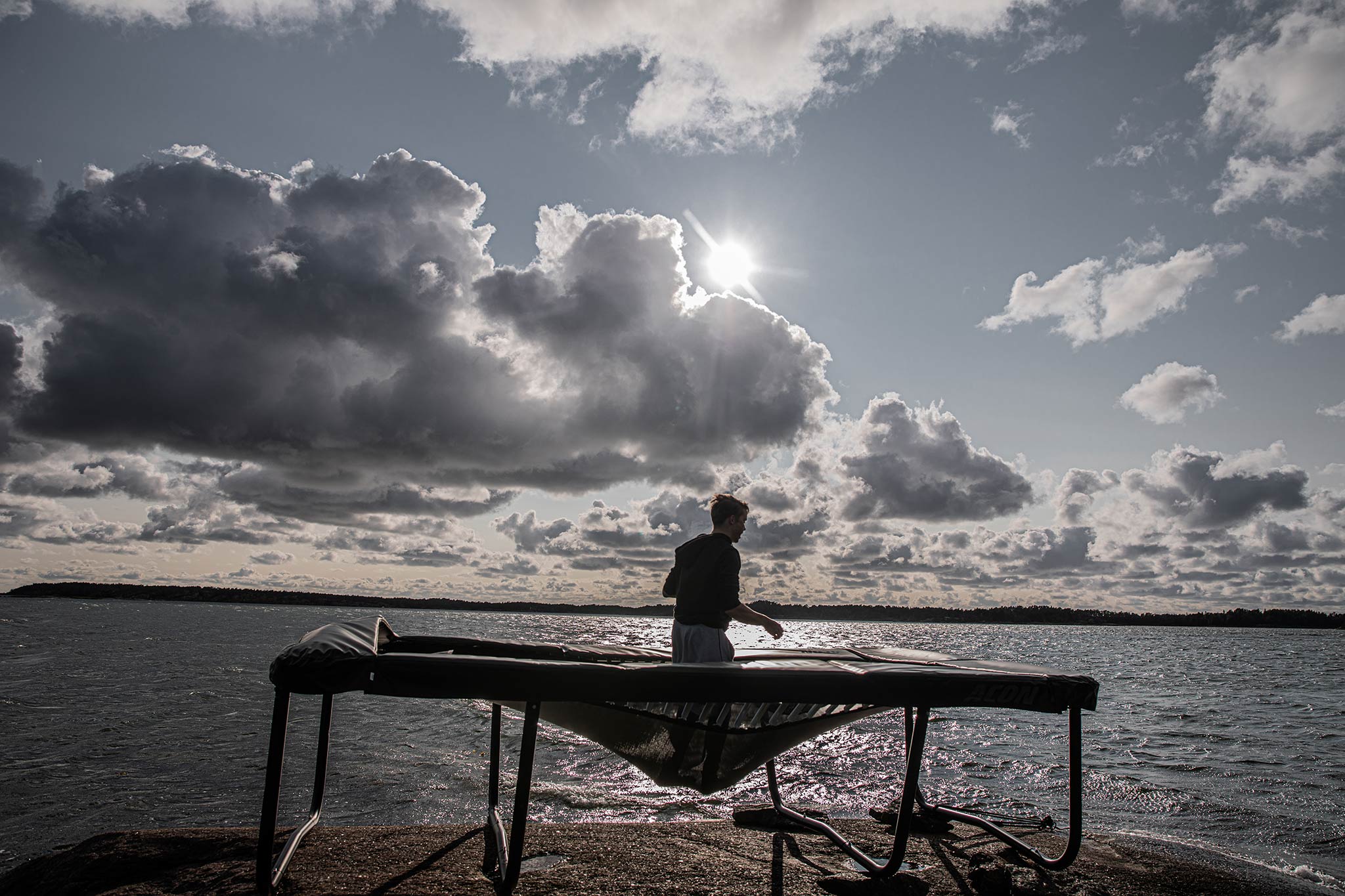 Trampoliinihyppääjä saaristomaisemassa vastavalossa