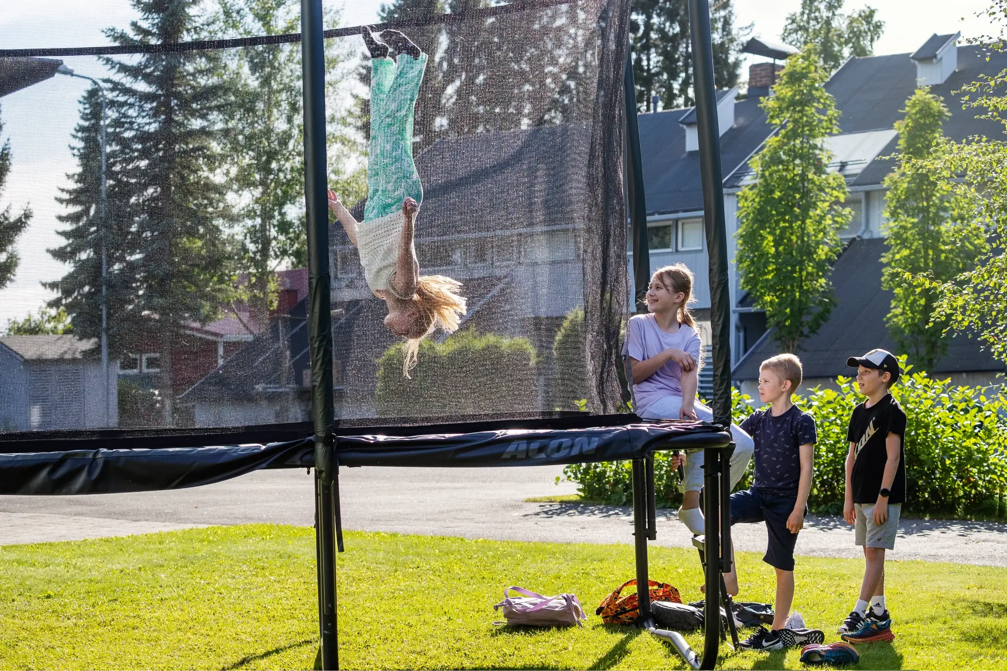 Lapsi tekee voltin trampoliinilla ystäviensä katsoessa vierestä.