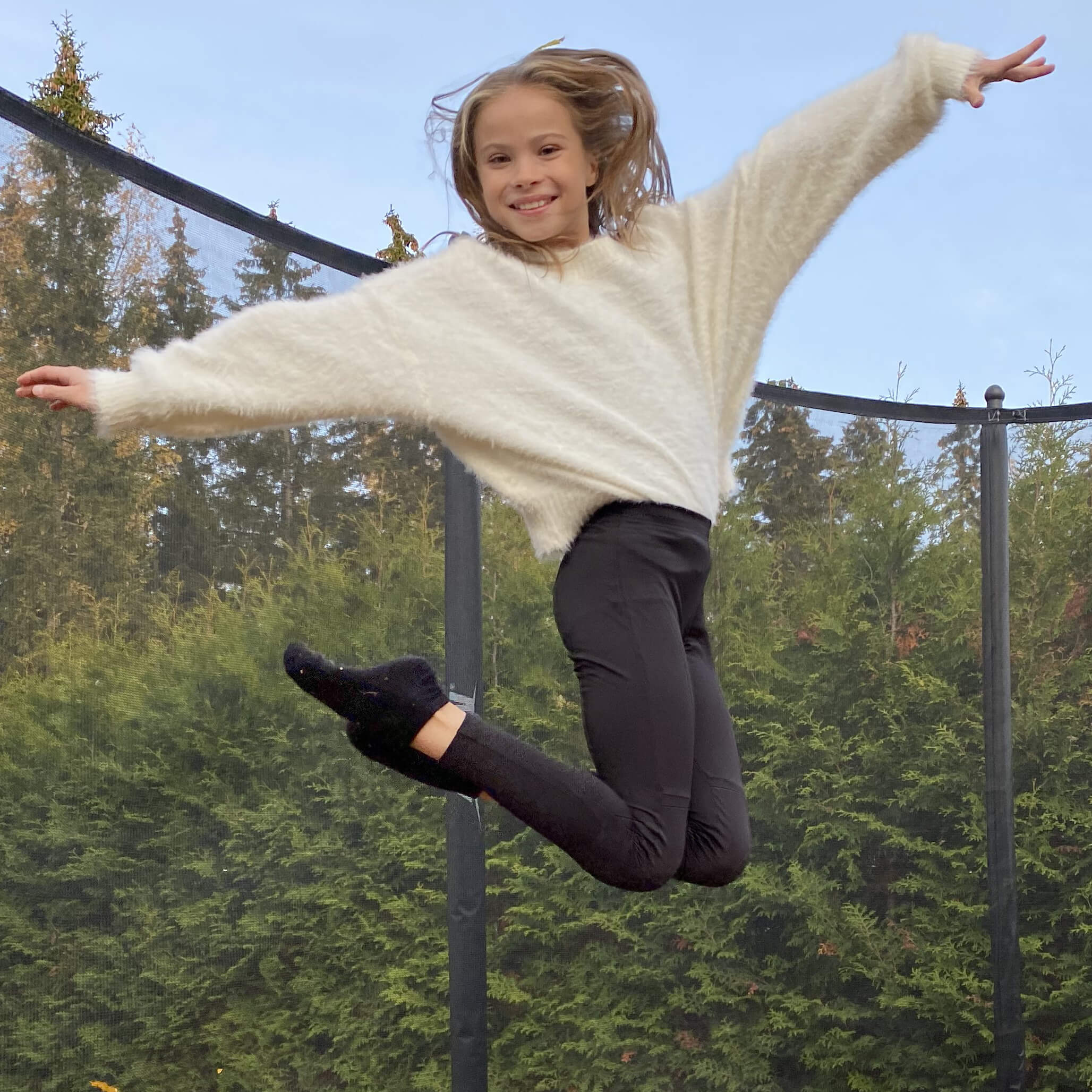 Hymyilevä tyttö hyppää trampoliinilla, turvaverkko taustalla