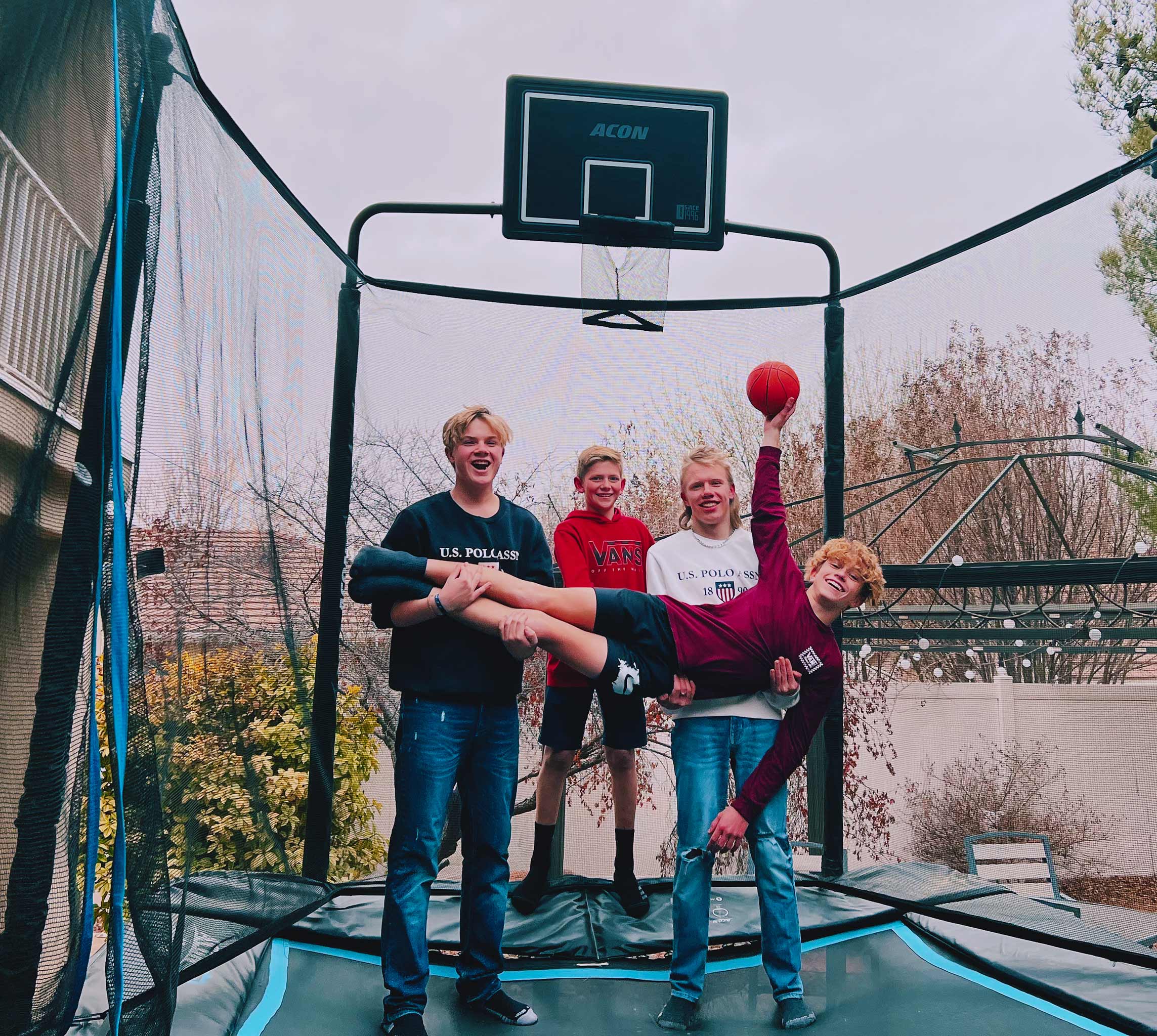 Kaverukset seisovat suorakulmaisella trampoliinilla, sylissä oleva poika pitelee trampoliinikoripalloa