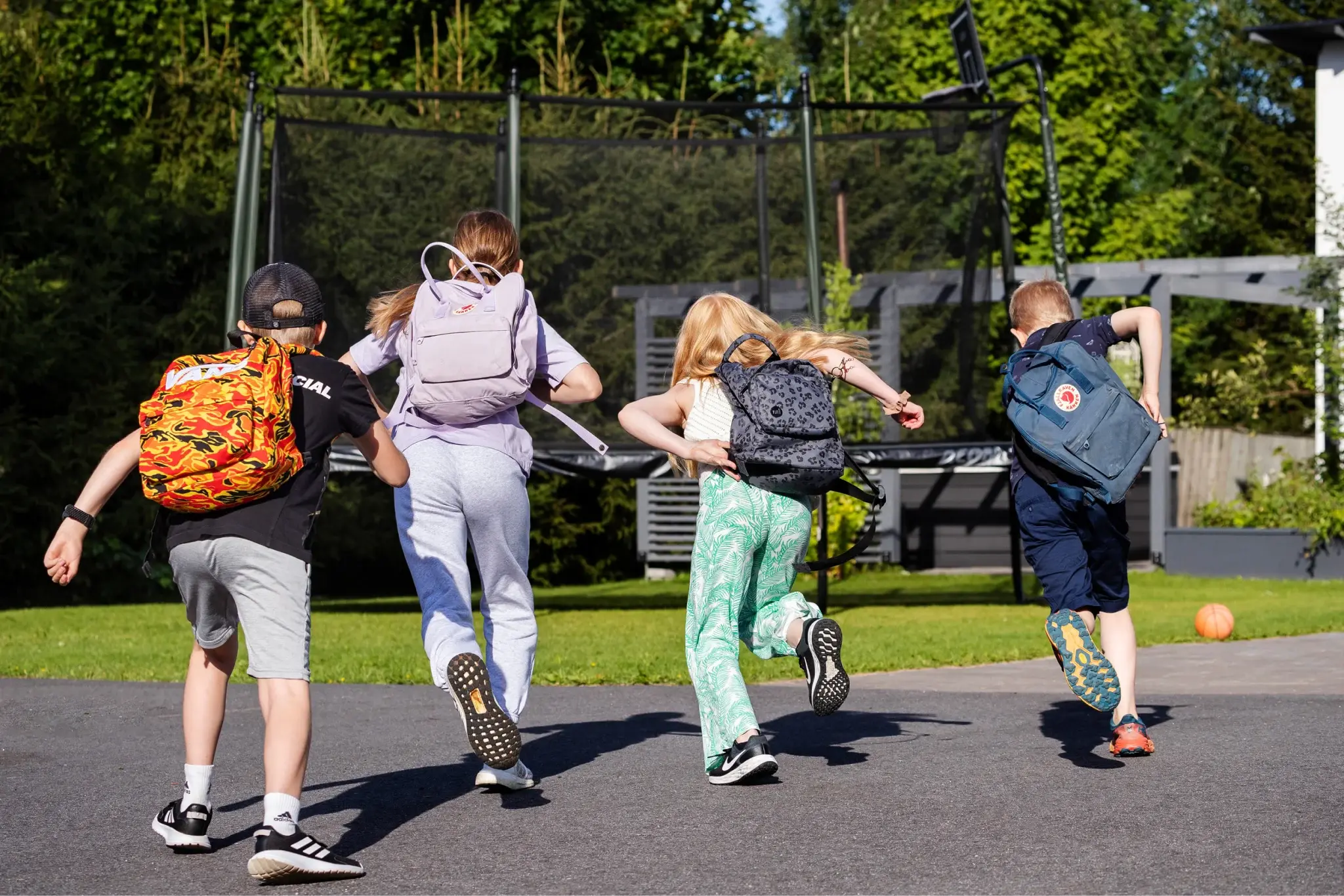 Neljä lasta reppu selässään juoksee kohti trampoliinia valmiina trampoliinipeleihin.