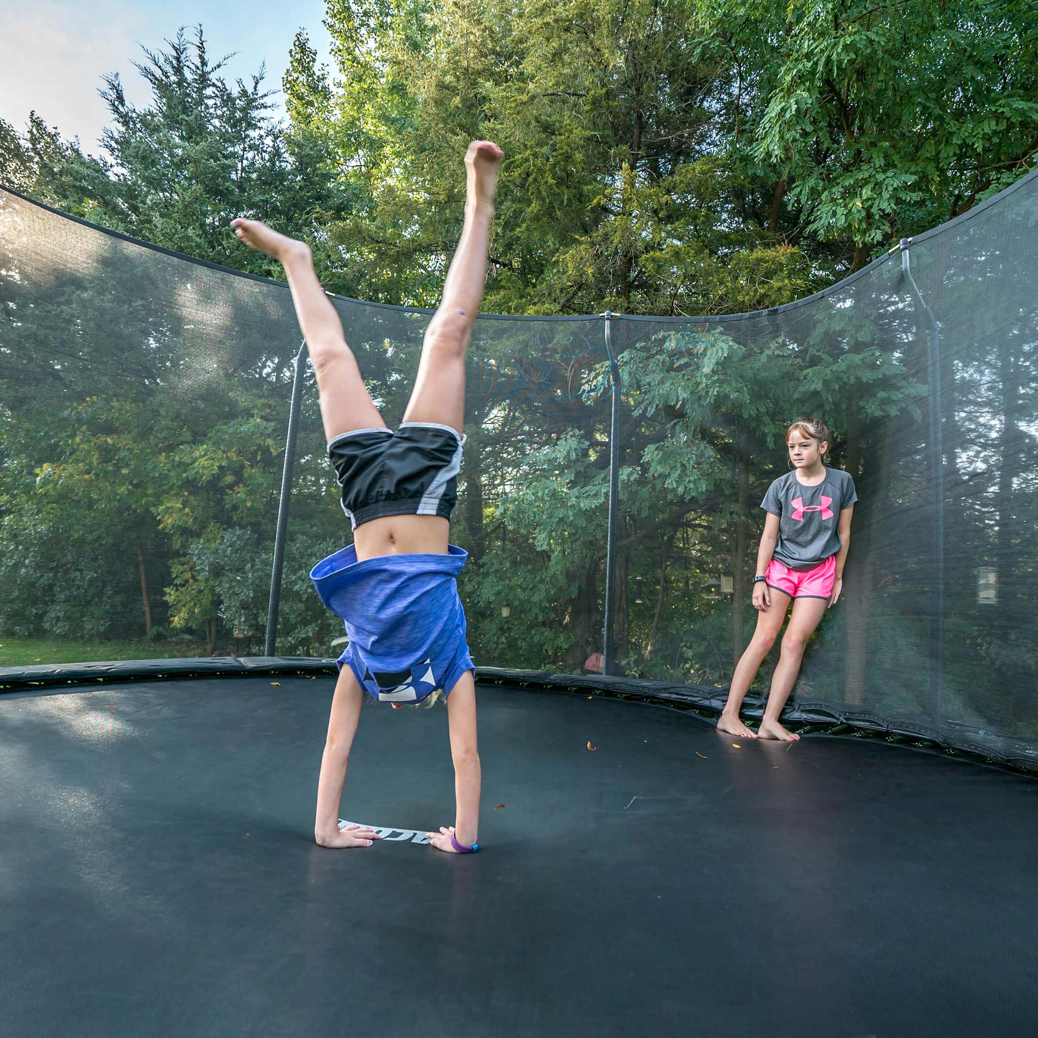 Tyttö seisoo käsillä Acon-trampoliinilla, ystävä katselee.