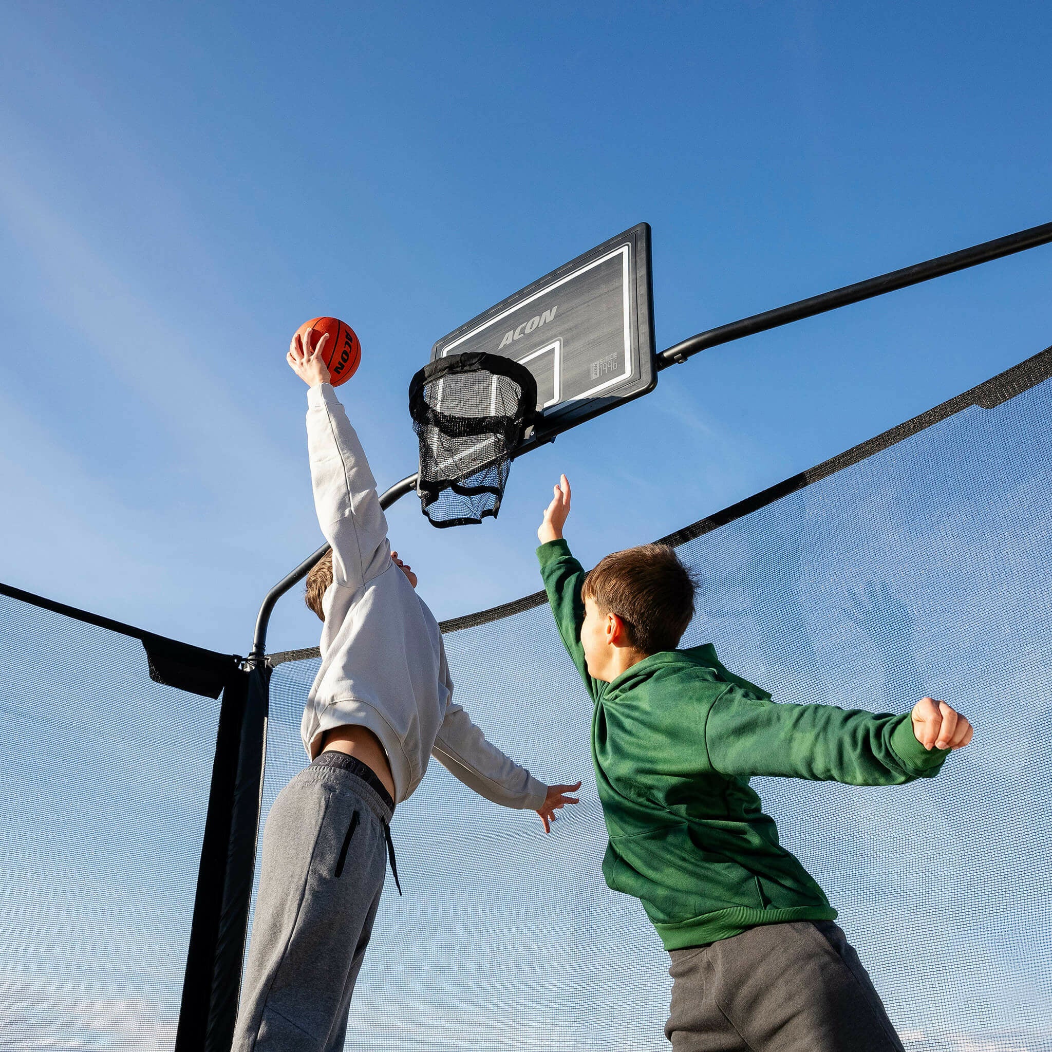 Kaksi poikaa pelaa koripalloa Acon X -trampoliinilla.