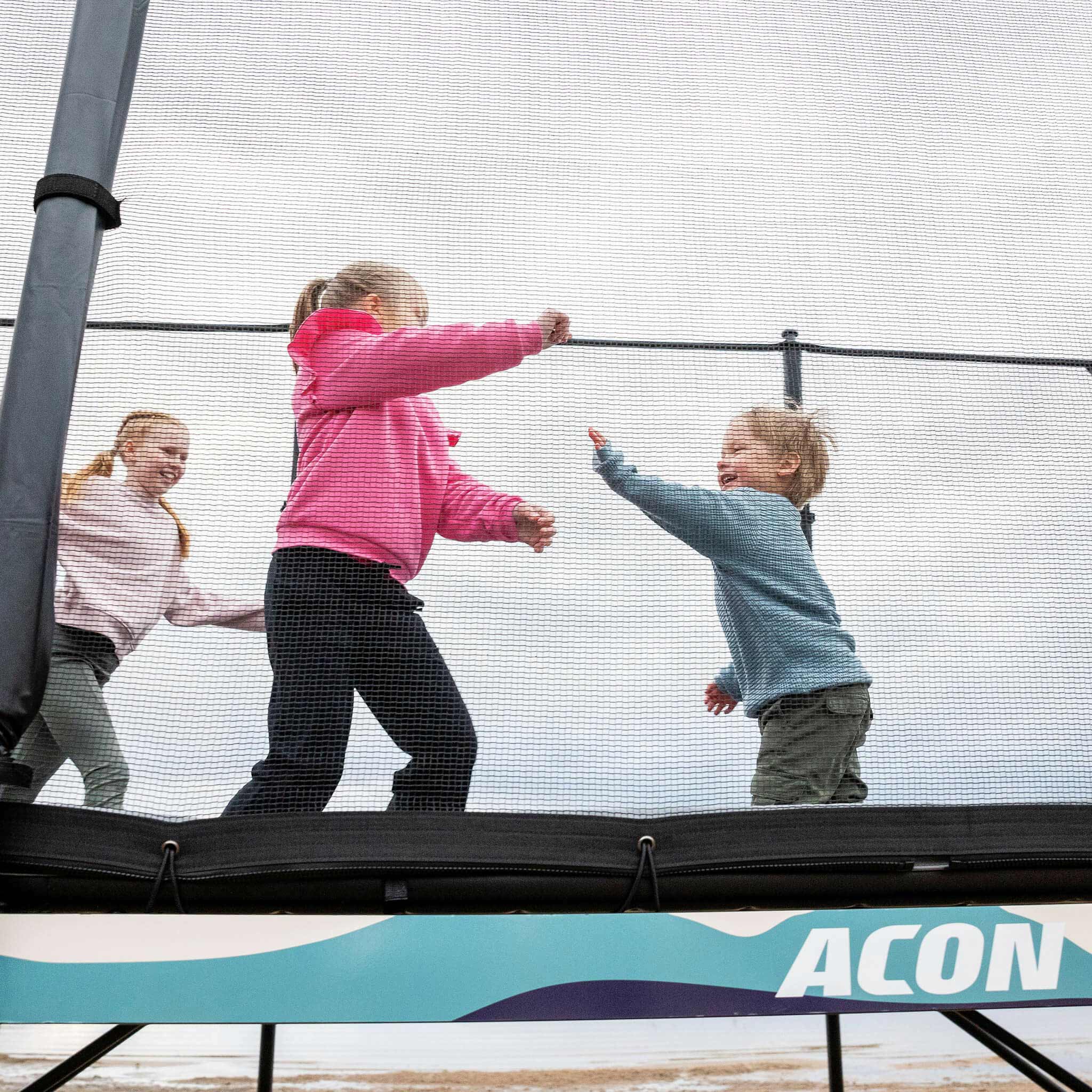 Kolme lasta leikkii Acon X -trampoliinilla.