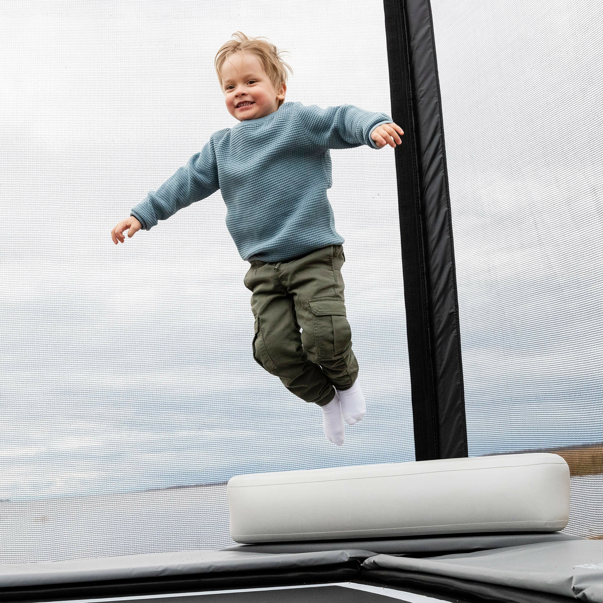 Pikkupoika hyppää Acon X Inflatable Triangle Blockin päältä trampoliinille.
