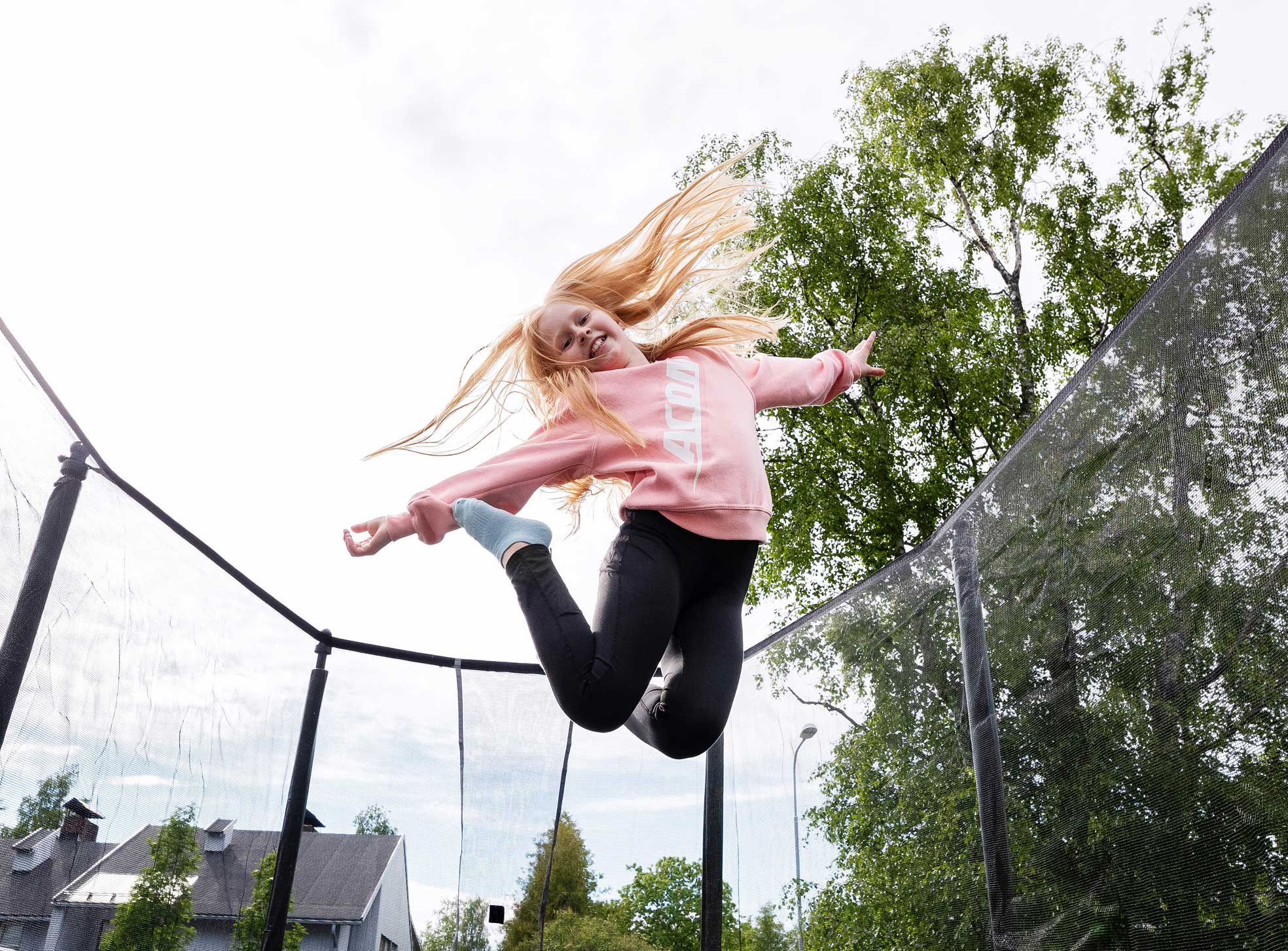 Vaaleahiuksinen tyttö hyppii hymyillen Acon trampoliinilla