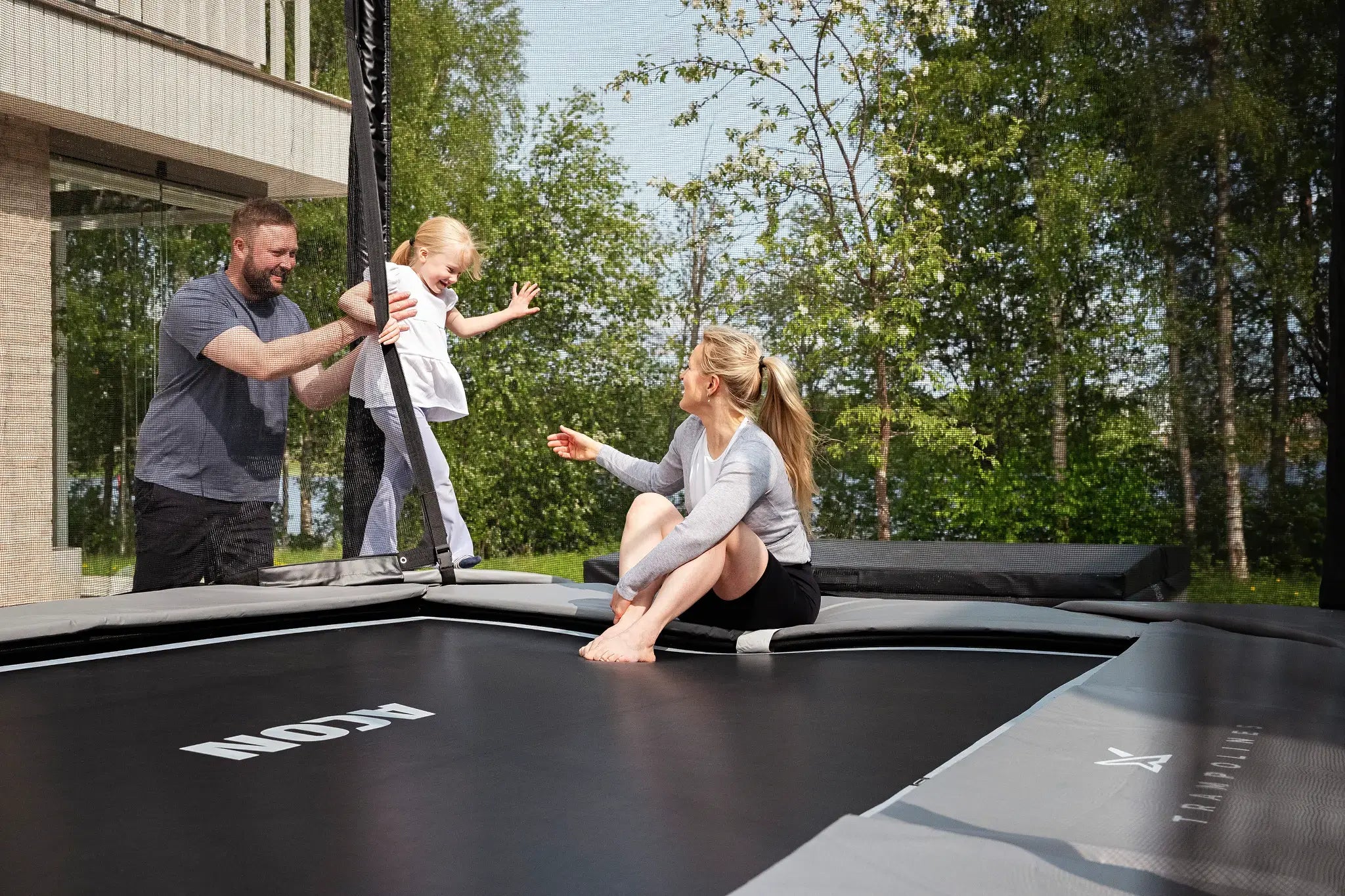 Vanhemmat ja pieni tyttö Acon trampoliinilla, jossa turvaverkko. 