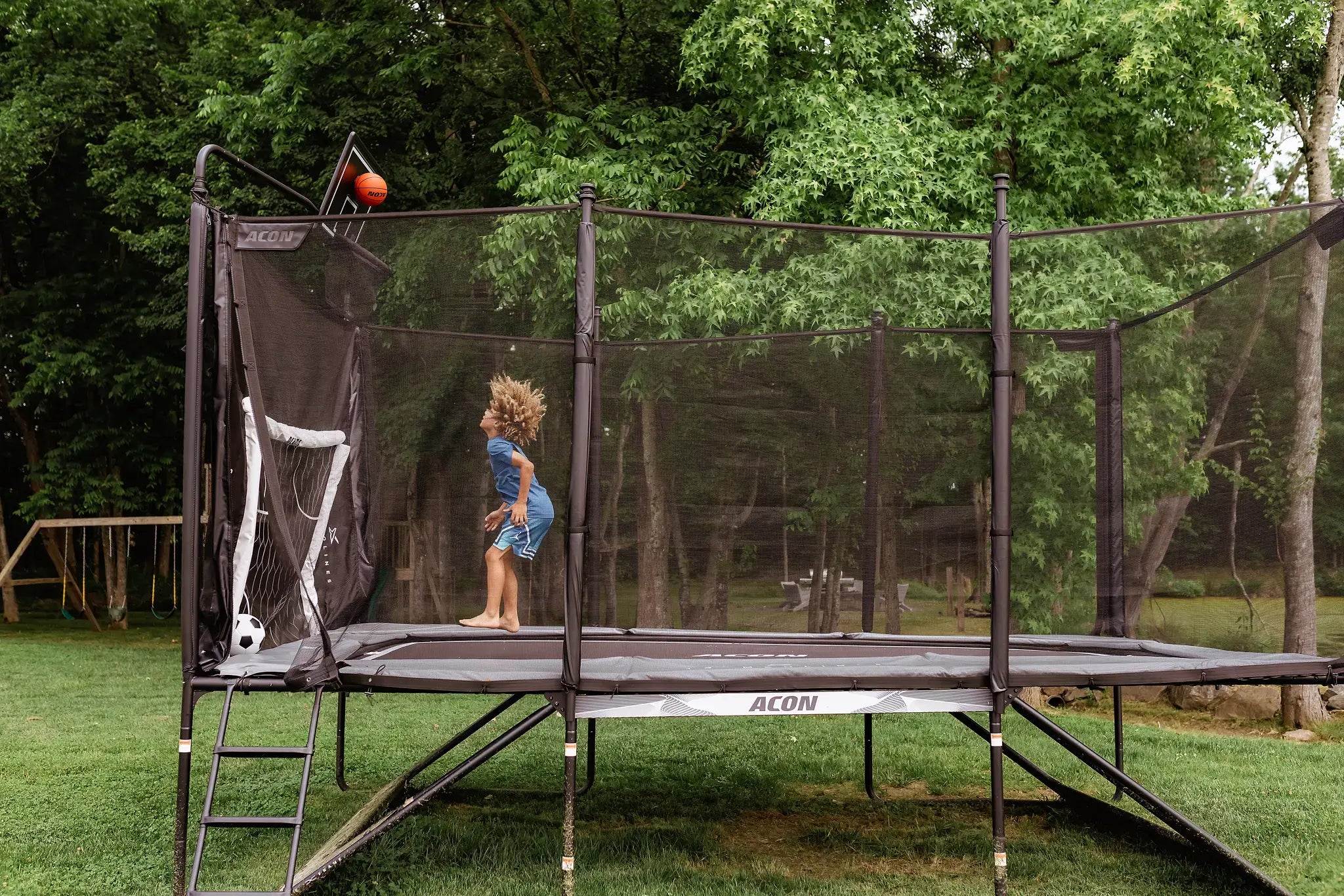 Lapsi leikkii Acon X trampoliinilla, jossa koripalloteline ja jalkapallomaali. 