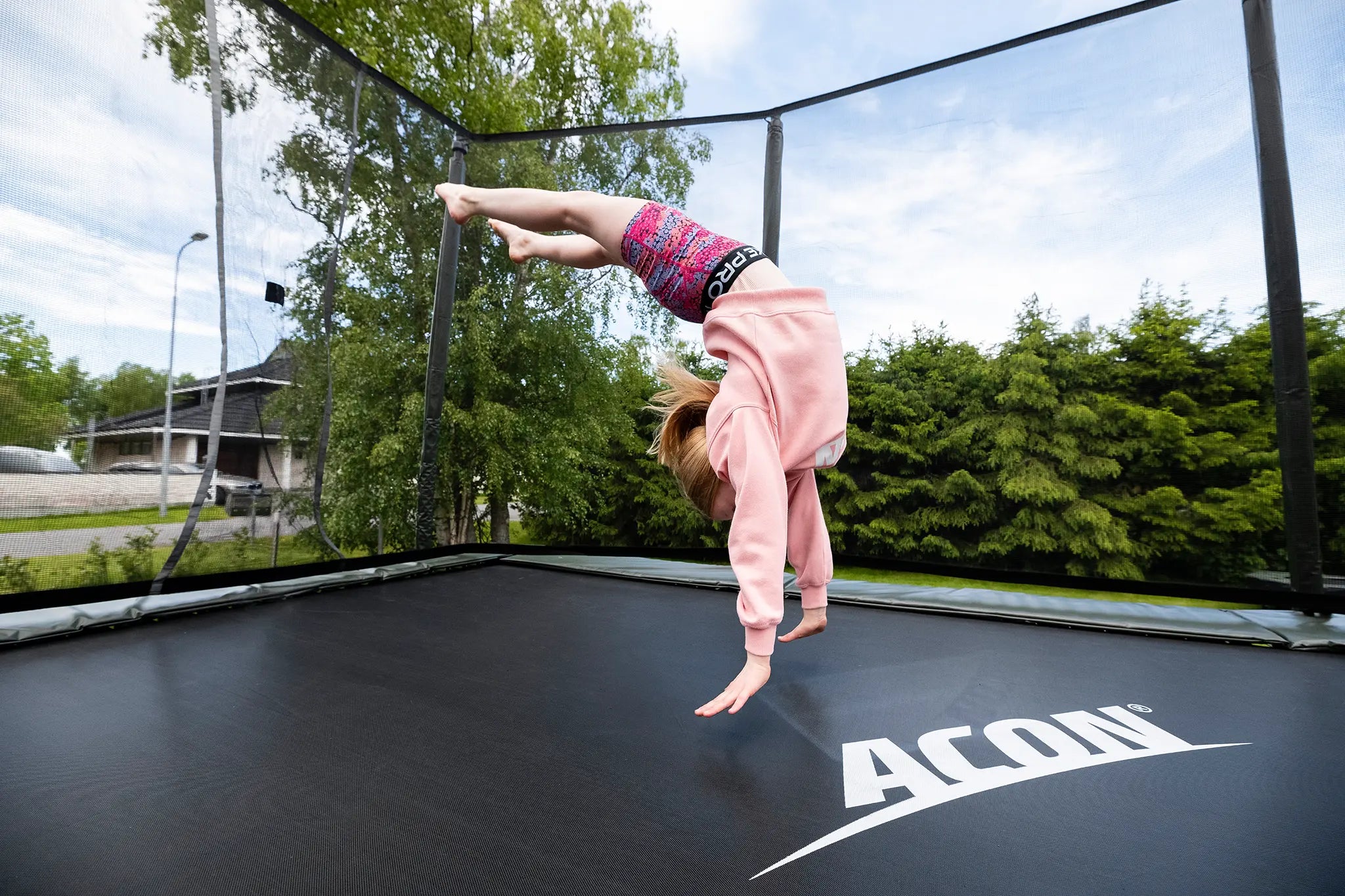 Tyttö tekee Aconin trampoliinilla tempun, laskeutuu kädet edellä maahan-