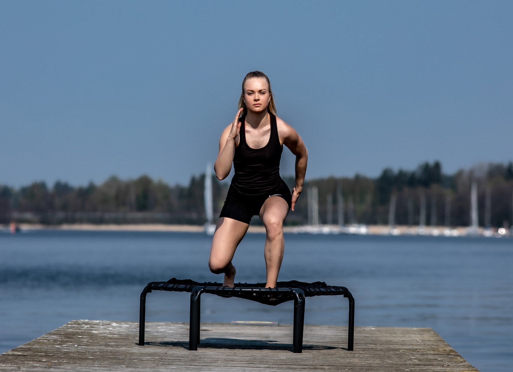 Nainen tekee askelkyykkyjä fitness trampoliinin päällä ulkona.