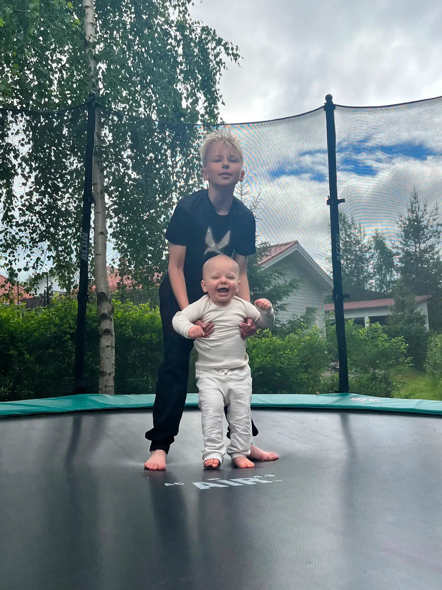 Nuori poika pitelemässä iloista vauvaa trampoliinilla.
