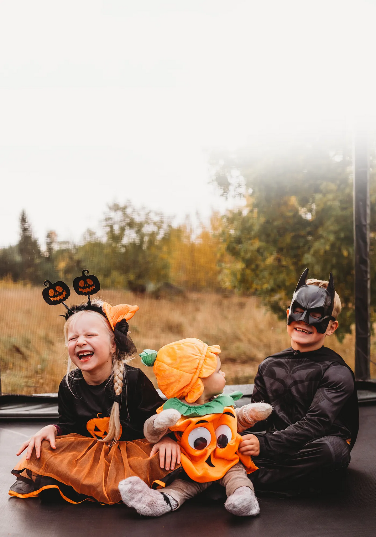 Kolme Halloween-asuihin pukeutunutta lasta istuu yhdessä ACON 16HD -trampoliinilla.