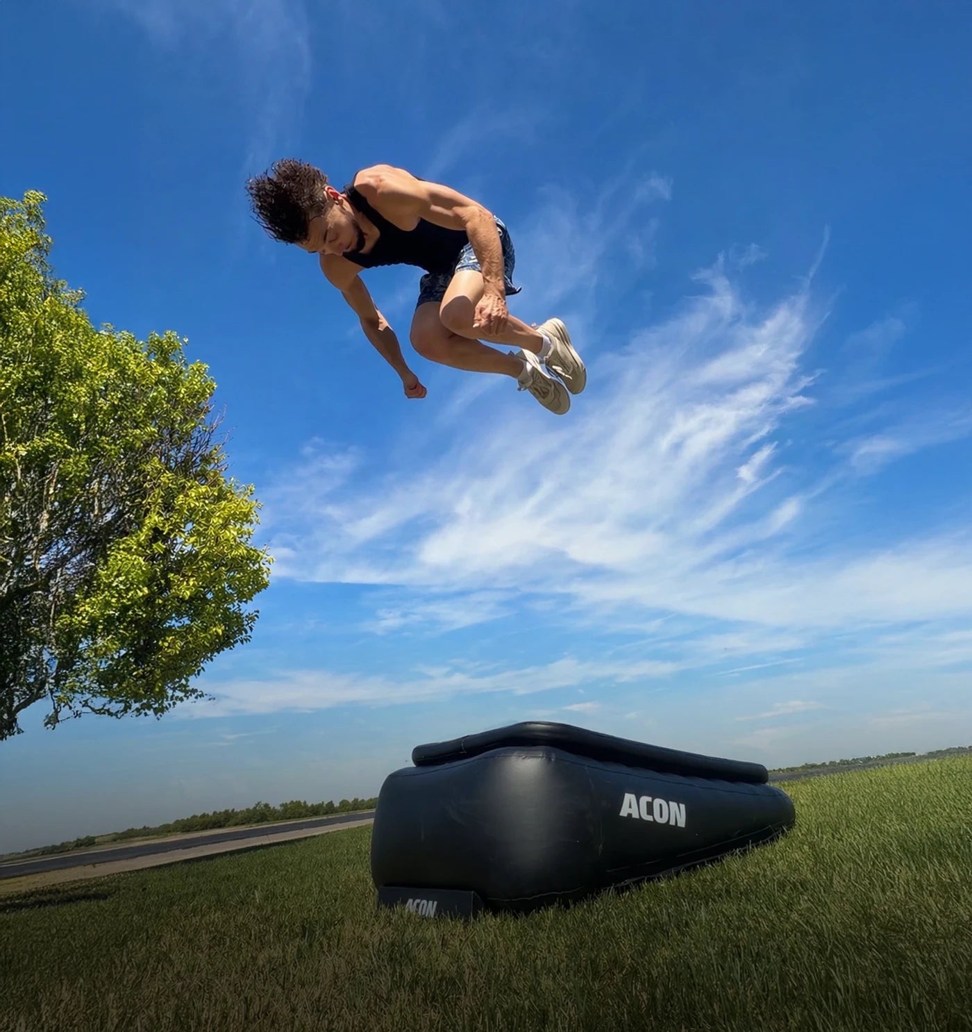 Mies hyppää korkean frontflipin Acon Airboardilla ulkona, Airboard nurmikolla.