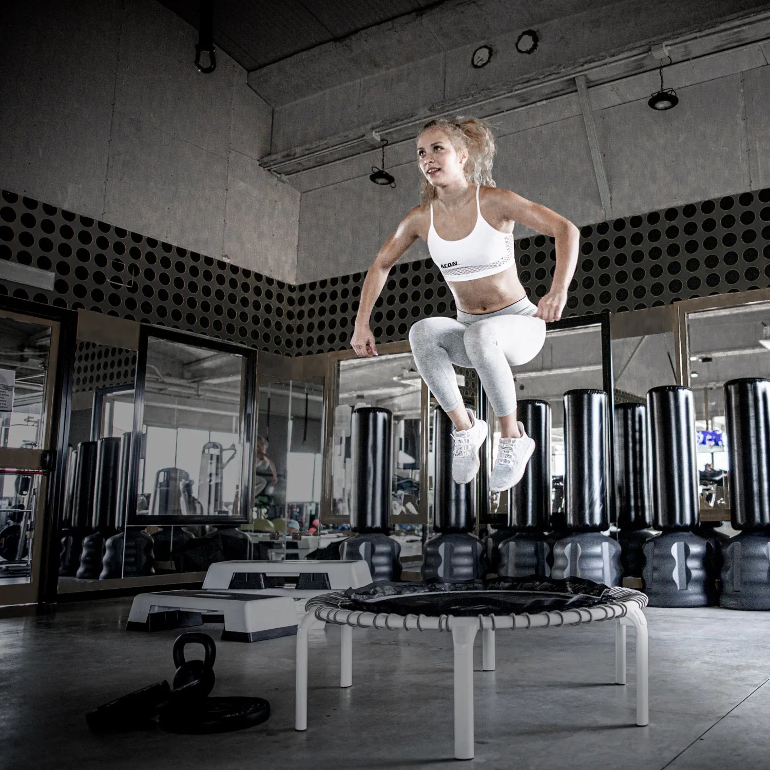 Urheilija hyppää ACON Fit 1,12 m Pyöreällä fitness-trampoliinilla Active-kahvatangolla kuntosalilla.