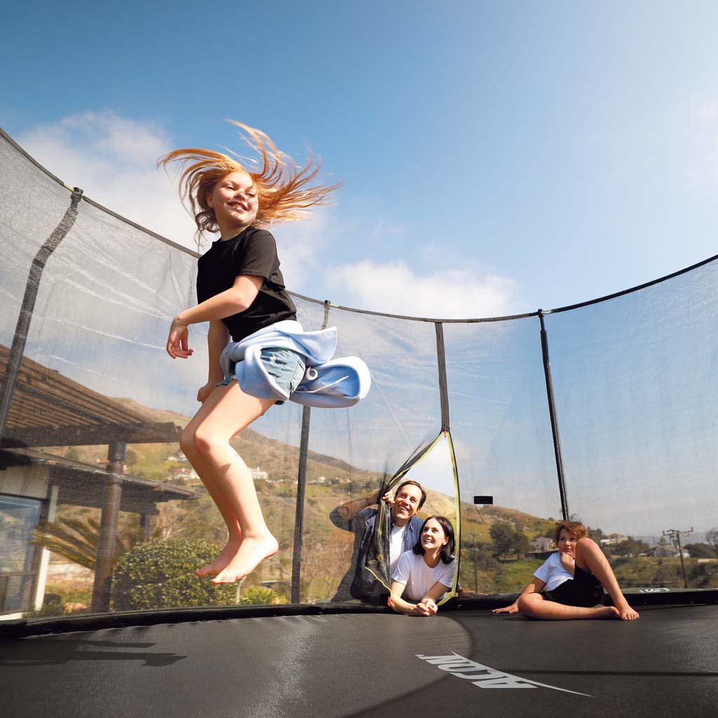 Tyttö hyppii trampoliinilla, perhe katselee