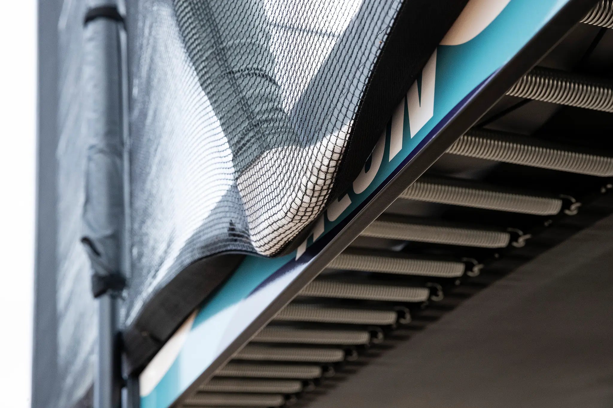 Lähikuvassa Acon X trampoliinin jouset ja henkilön jalka turvaverkkoa vasten.