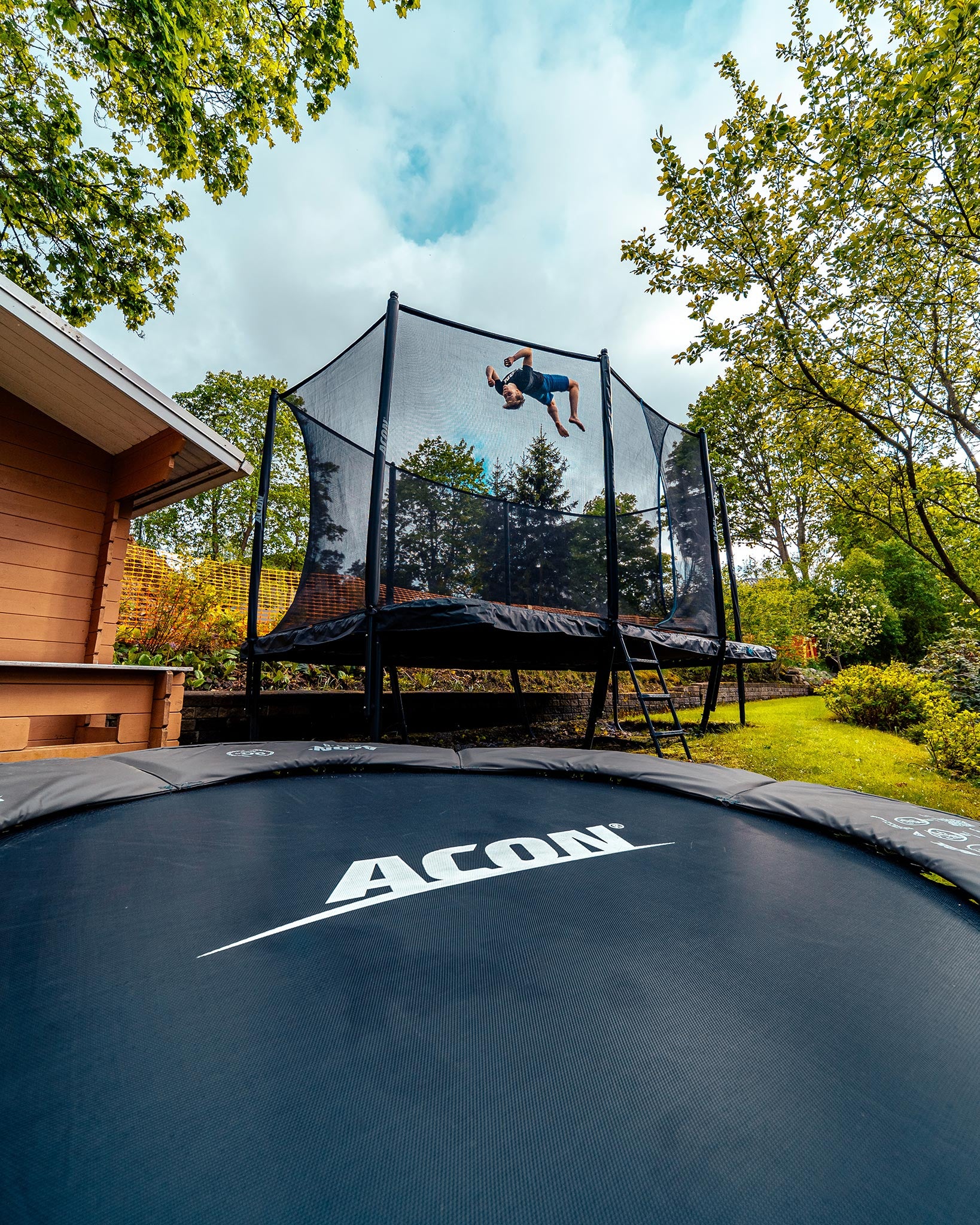 Poika hyppää voltin 16 HD trampoliinilla kesäisessä puutarhassa