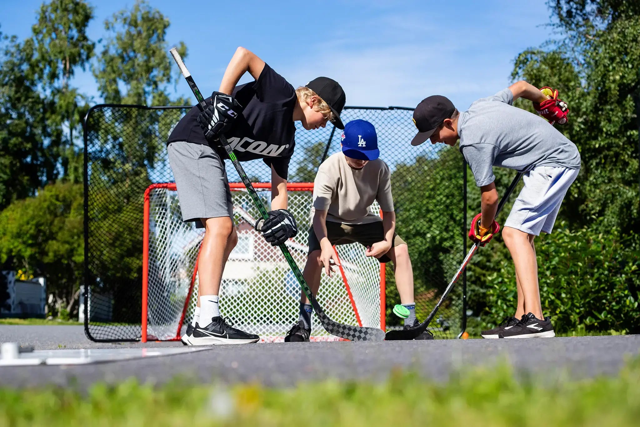 Nuoret pelaamassa pihajääkiekkoa kesäisellä pihatiellä.