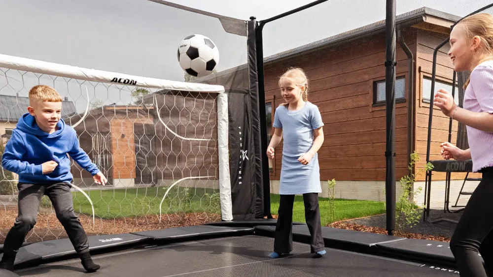 Lapset pelaavat jalkapalloa Acon X -trampoliinilla, jossa on ACON Soccer Goal.
