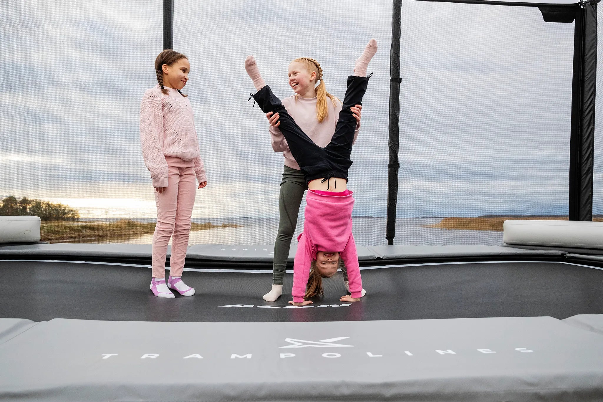 Kolme tyttöä Aconin trampoliinilla, jossa on turvaverkko.