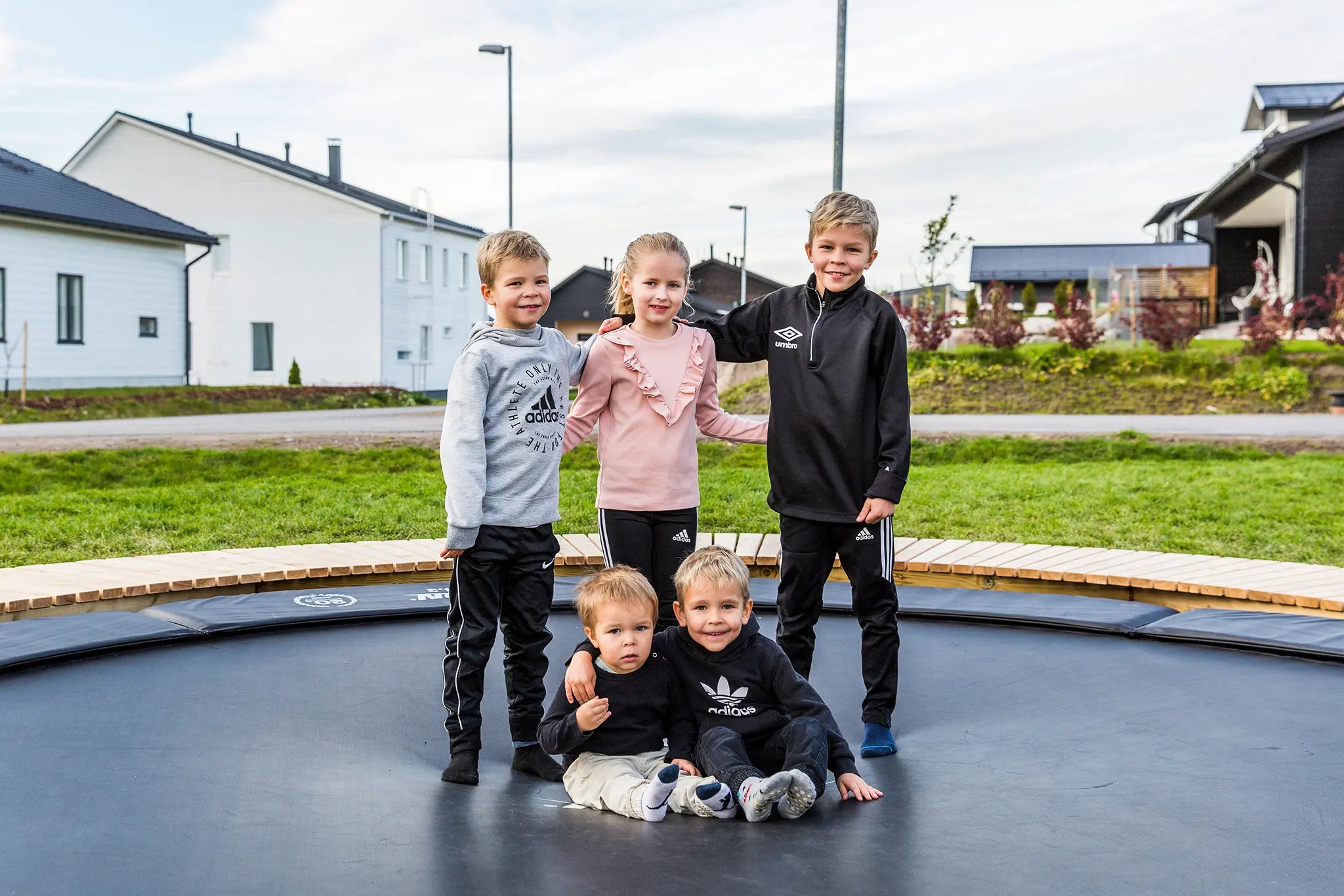 Kolme lasta seisoo ja kaksi istuu Aconin maahan upotetulla trampoliinilla. 