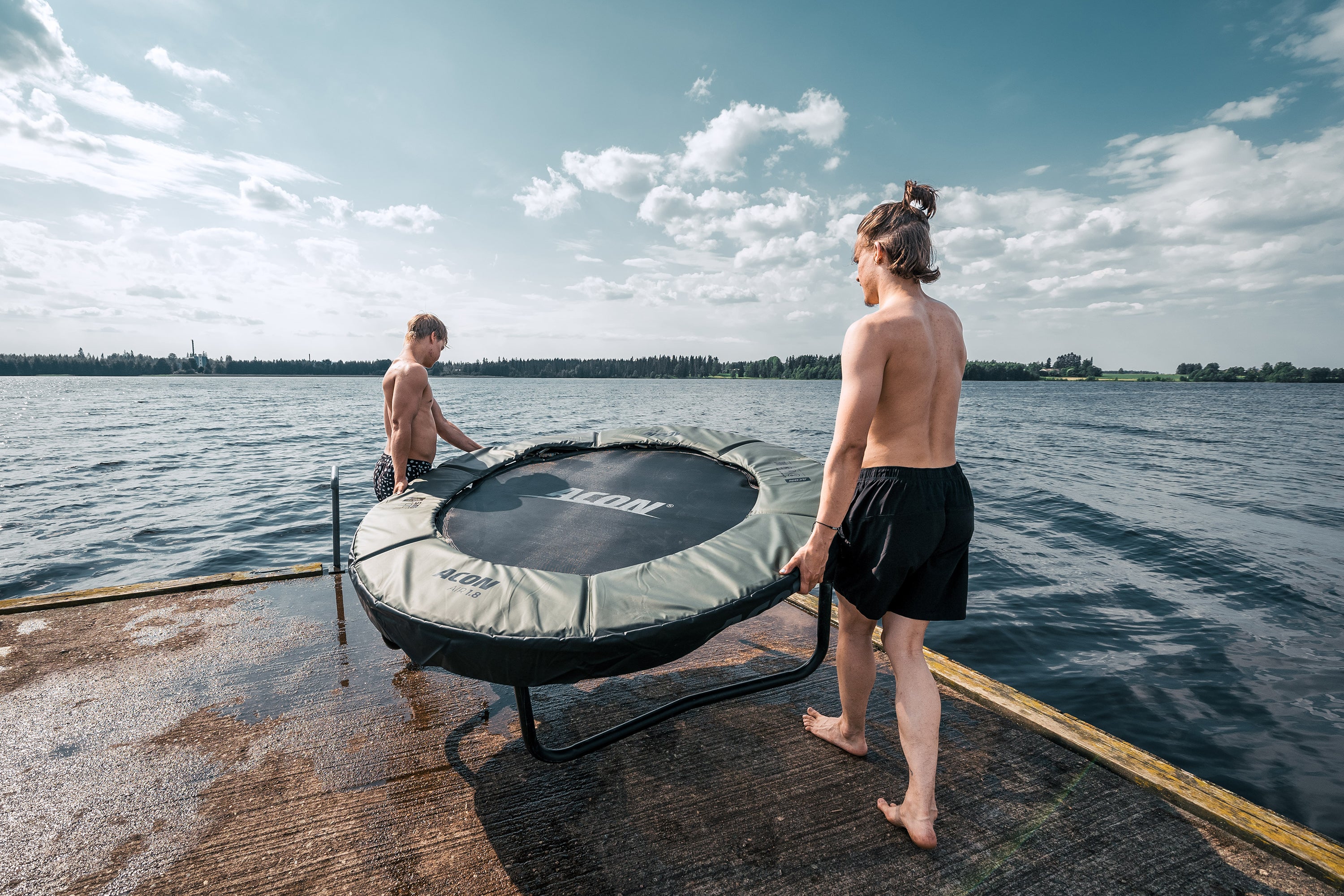 Kaksi poikaa kantaa Aconin minitrampoliinia laiturilla järvenrannassa.