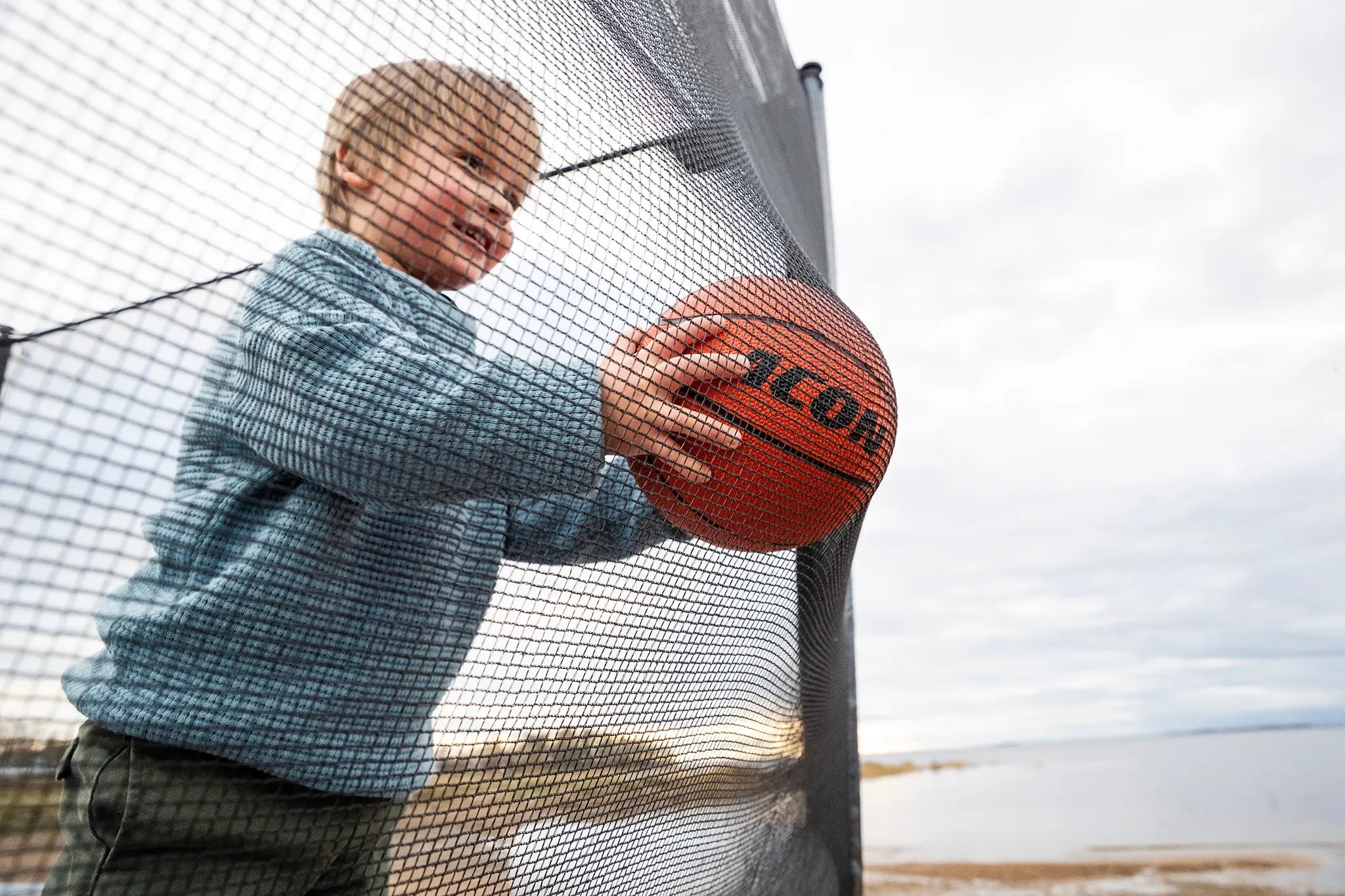Poika Aconin trampoliinilla, työntää koripalloa turvaverkkoa kohti. 