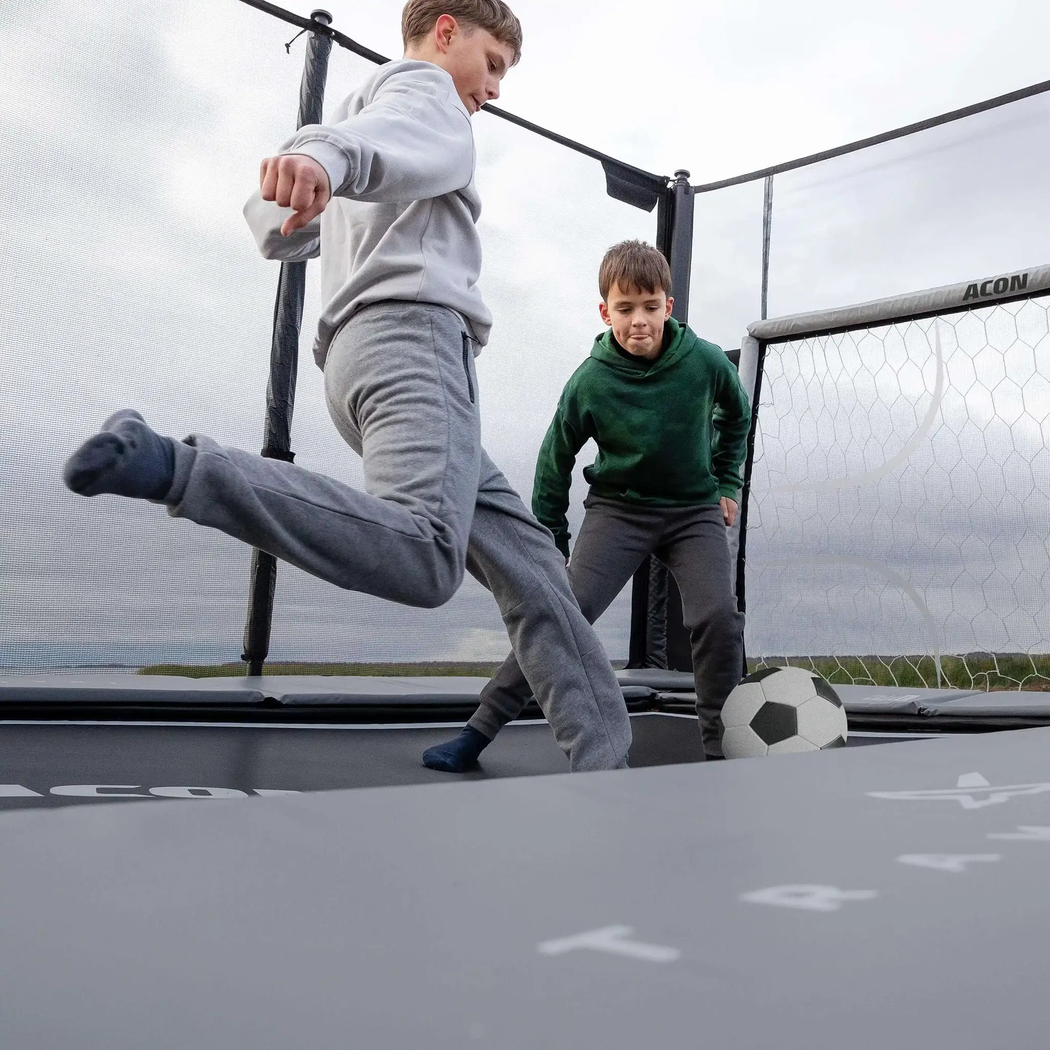 Kaksi poikaa pelaa jalkapalloa Acon X trampoliinilla.