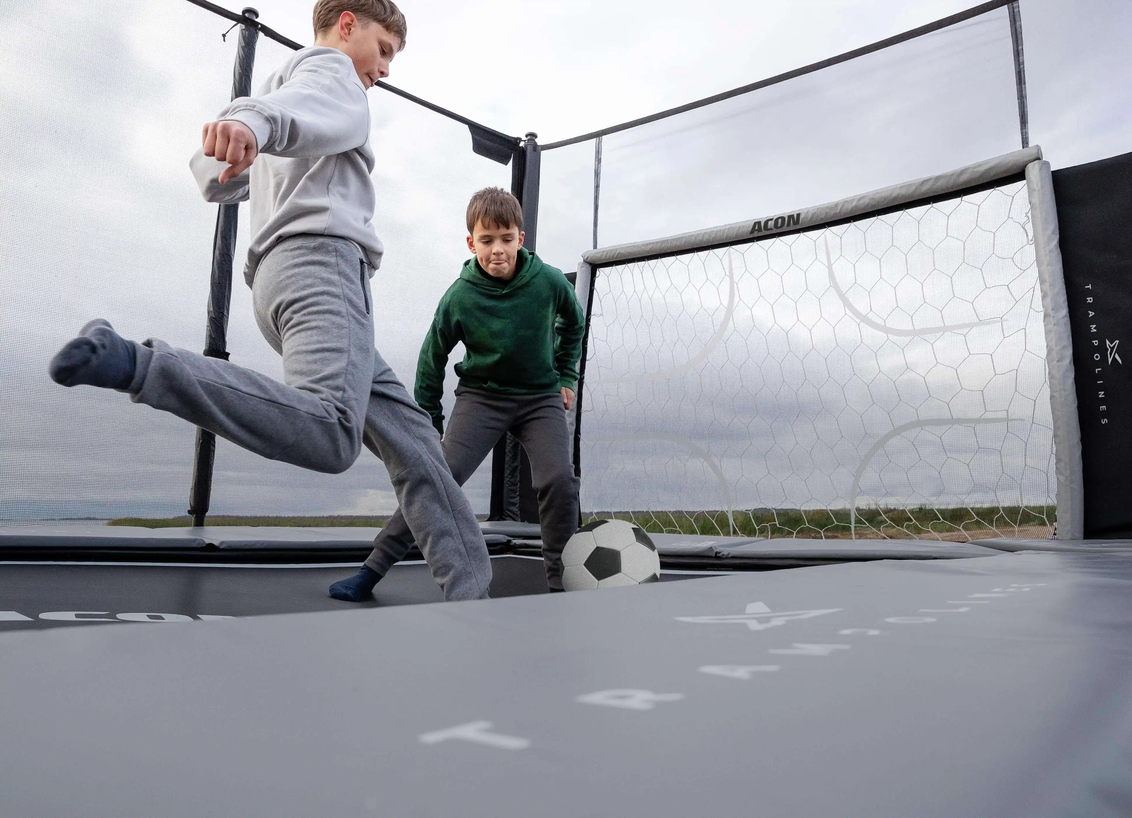 Kaksi poikaa pelaamassa jalkapalloa Acon X 17 trampoliinilla.