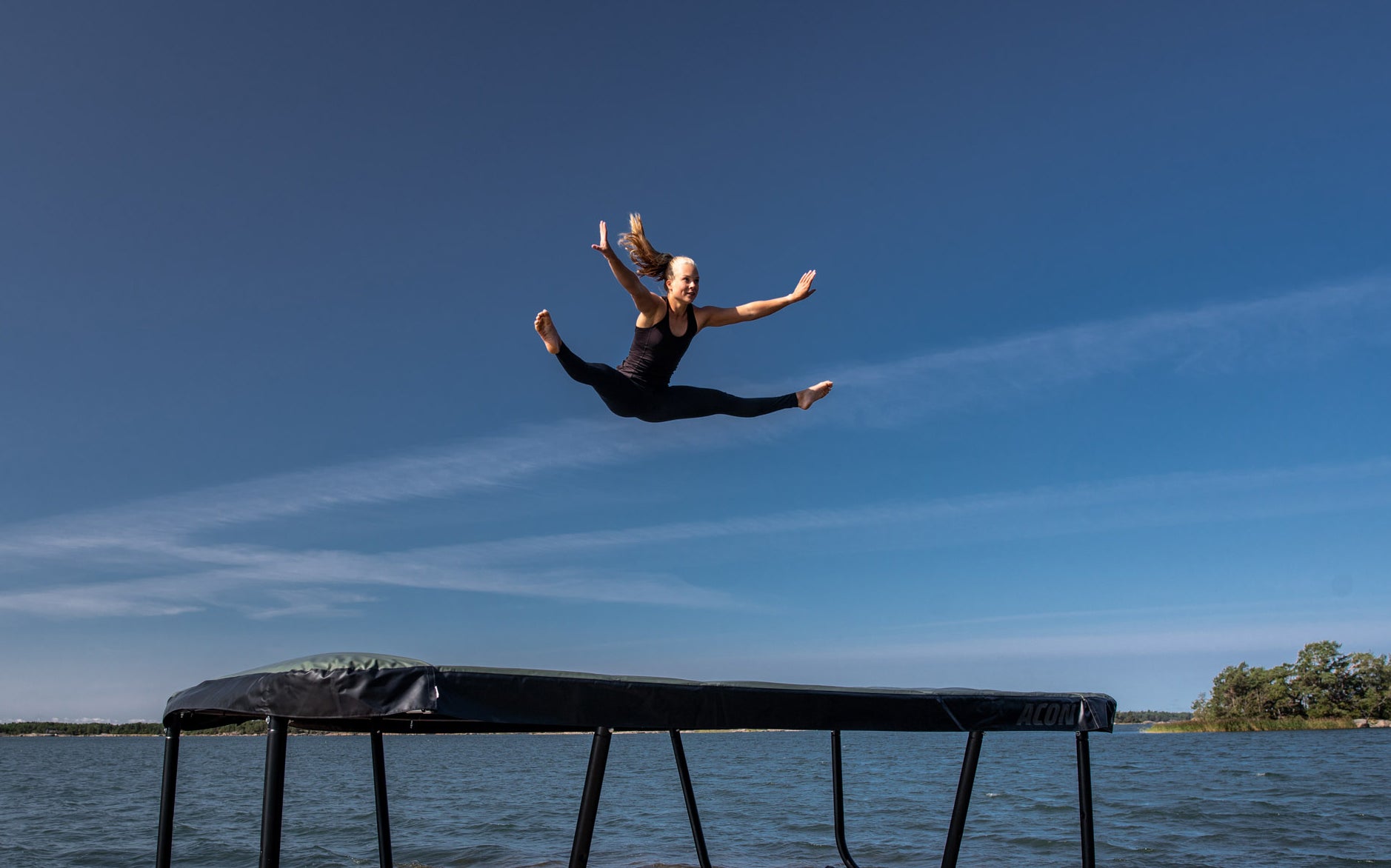 Nainen hyppää Acon 13HD trampoliinilla kesäisessä saaristomaisemassa