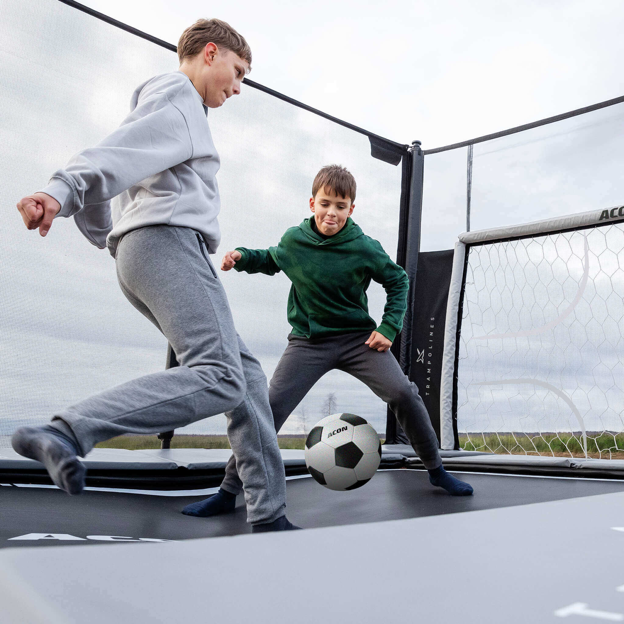 Kaksi poikaa pelaa jalkapalloa Acon X 17 -trampoliinilla, jossa on jalkapallomaali
