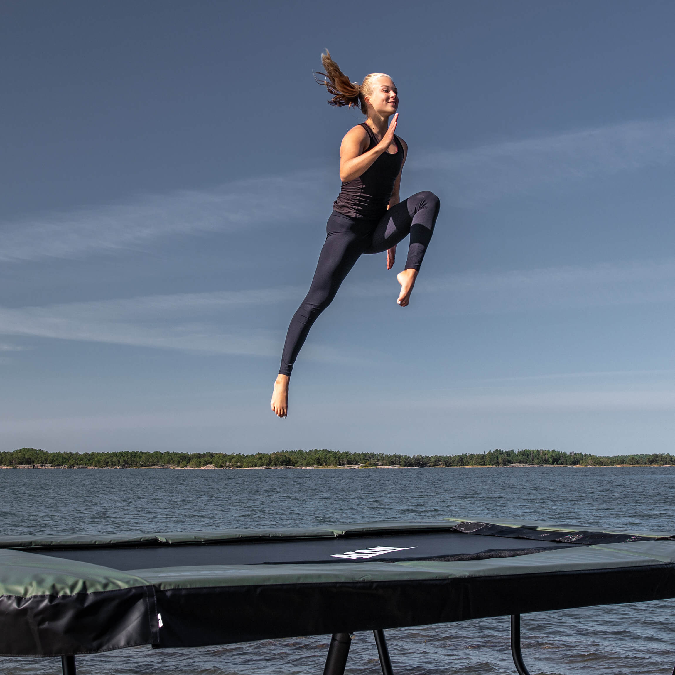 Voimistelija hyppää Acon 13 Sport HD -trampoliinilla saaristomaisemassa.