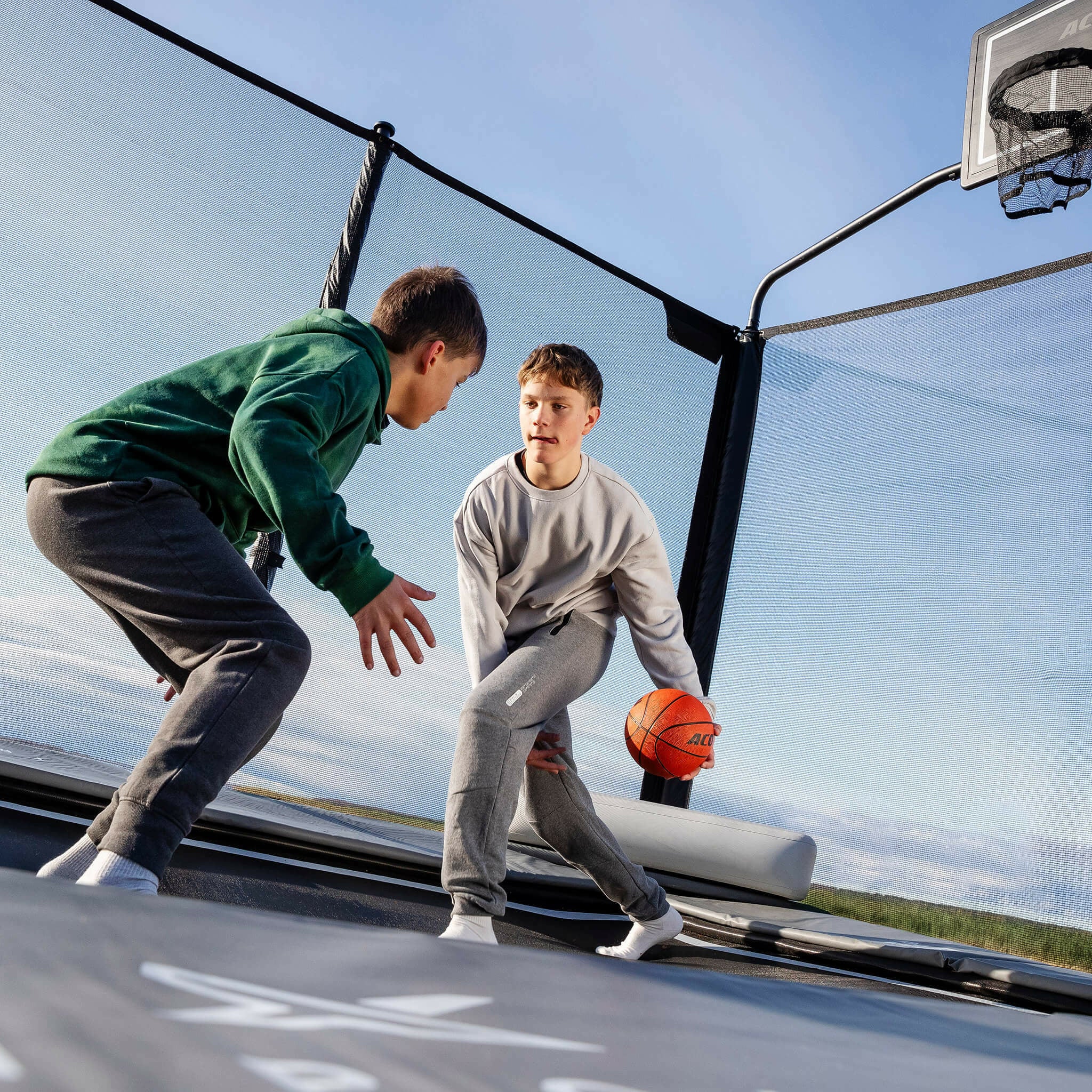 Kaksi poikaa pelaamassa koripalloa Acon X -trampoliinilla.